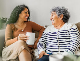 A woman and her mother smile at each other on a couch.