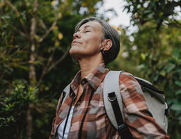 A woman hiking pauses for breath, eyes closed.